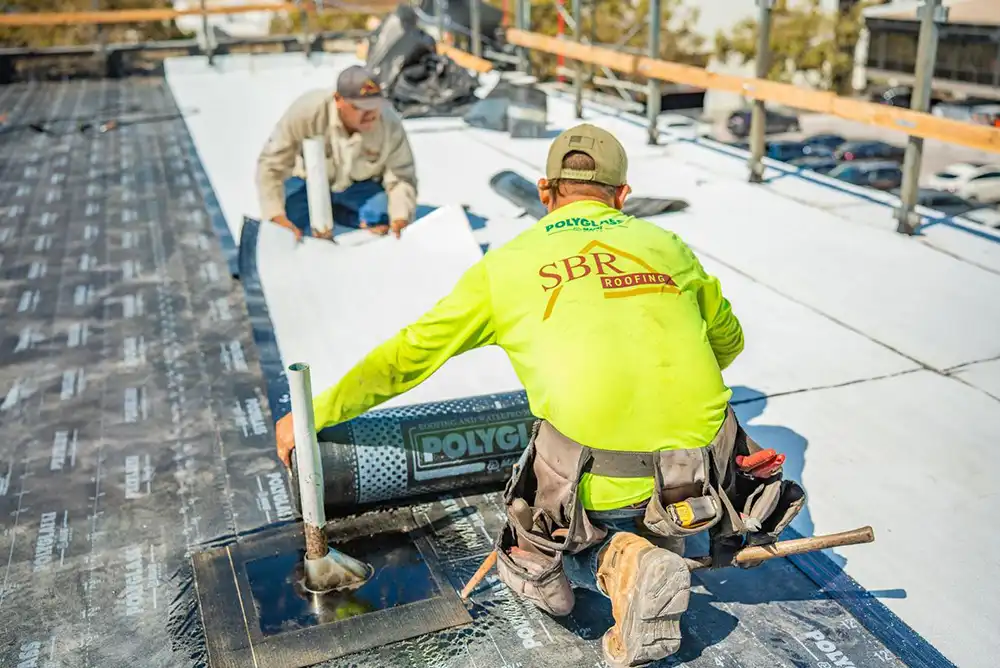 Two SBR Roofing professionals laying roofing material on a commercial flat roof