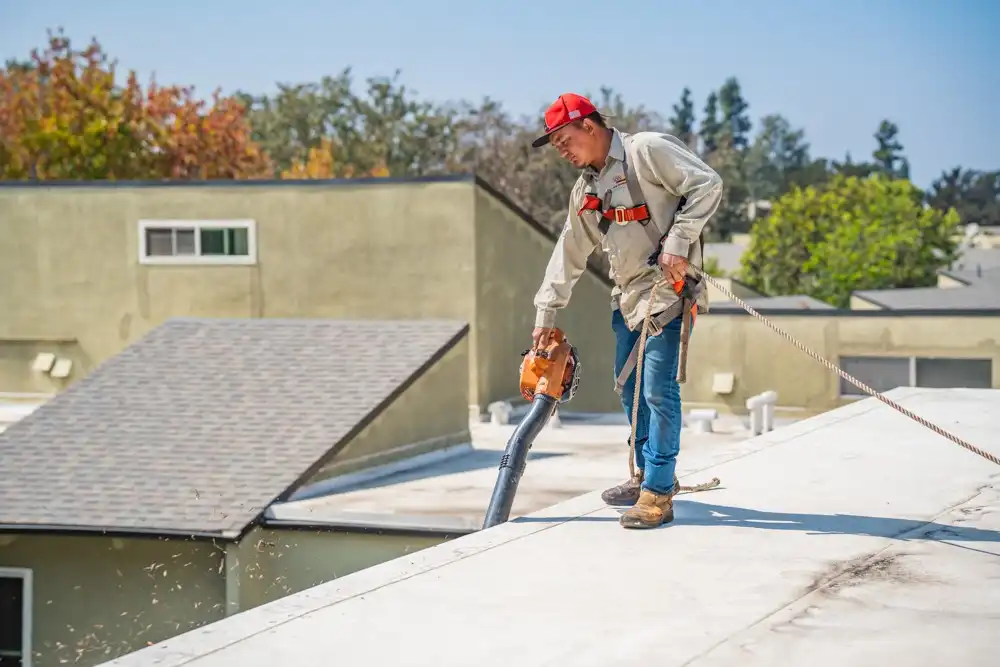 a commercial roof contractor cleaning the leaves out of the gutters of a commercial flat roof